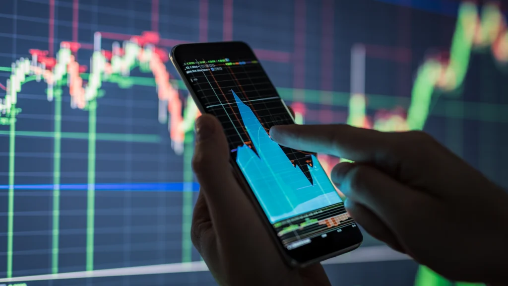 person looking at stock market graph on a mobile phone app and computer monitor