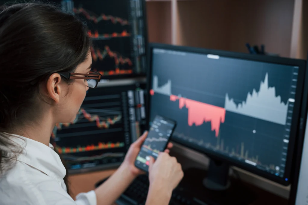 woman looking at indices trading charts on mobile trading app and monitor screen