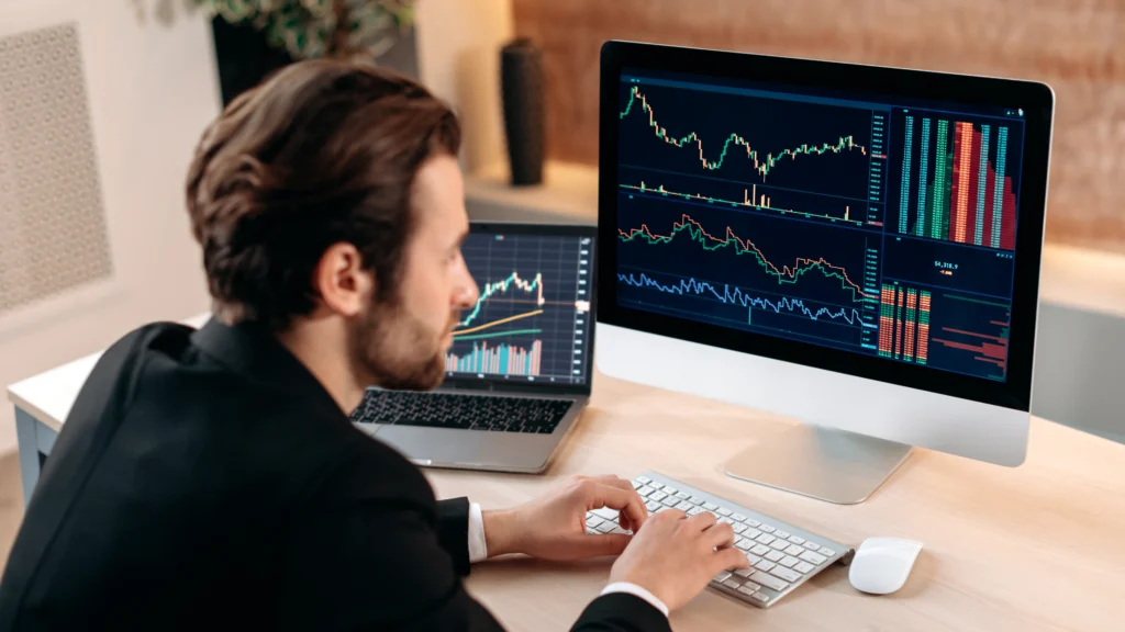 indices-trader-looking-at-many-financial-market-charts-on-computer-monitor-and-a-laptop